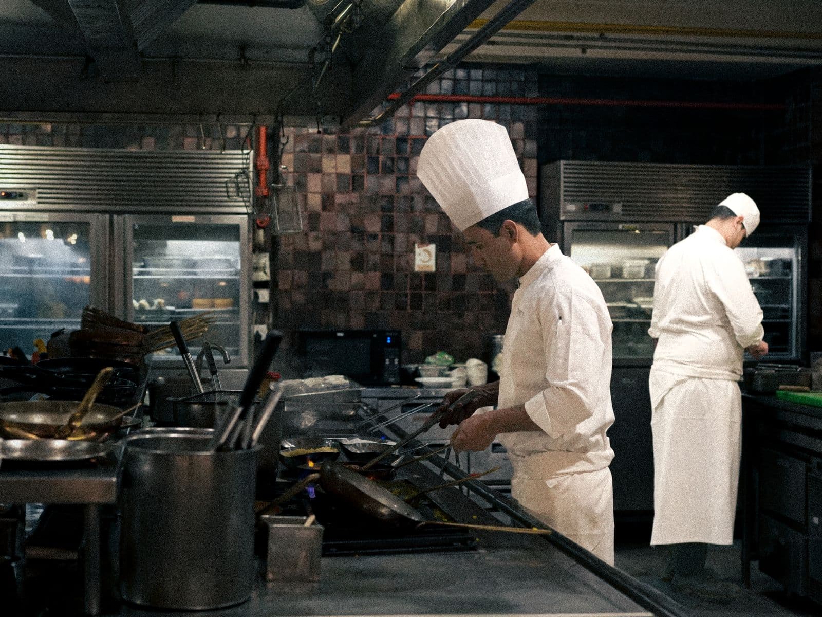 Deux chefs en tenue blanche au travail dans une cuisine professionnelle en inox